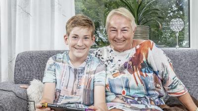 Oma draagt ata personenalarmering, kleinzoon zit naast haar op de bank